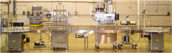 A stainless steel industrial bottling or packaging machine line situated in a factory setting.