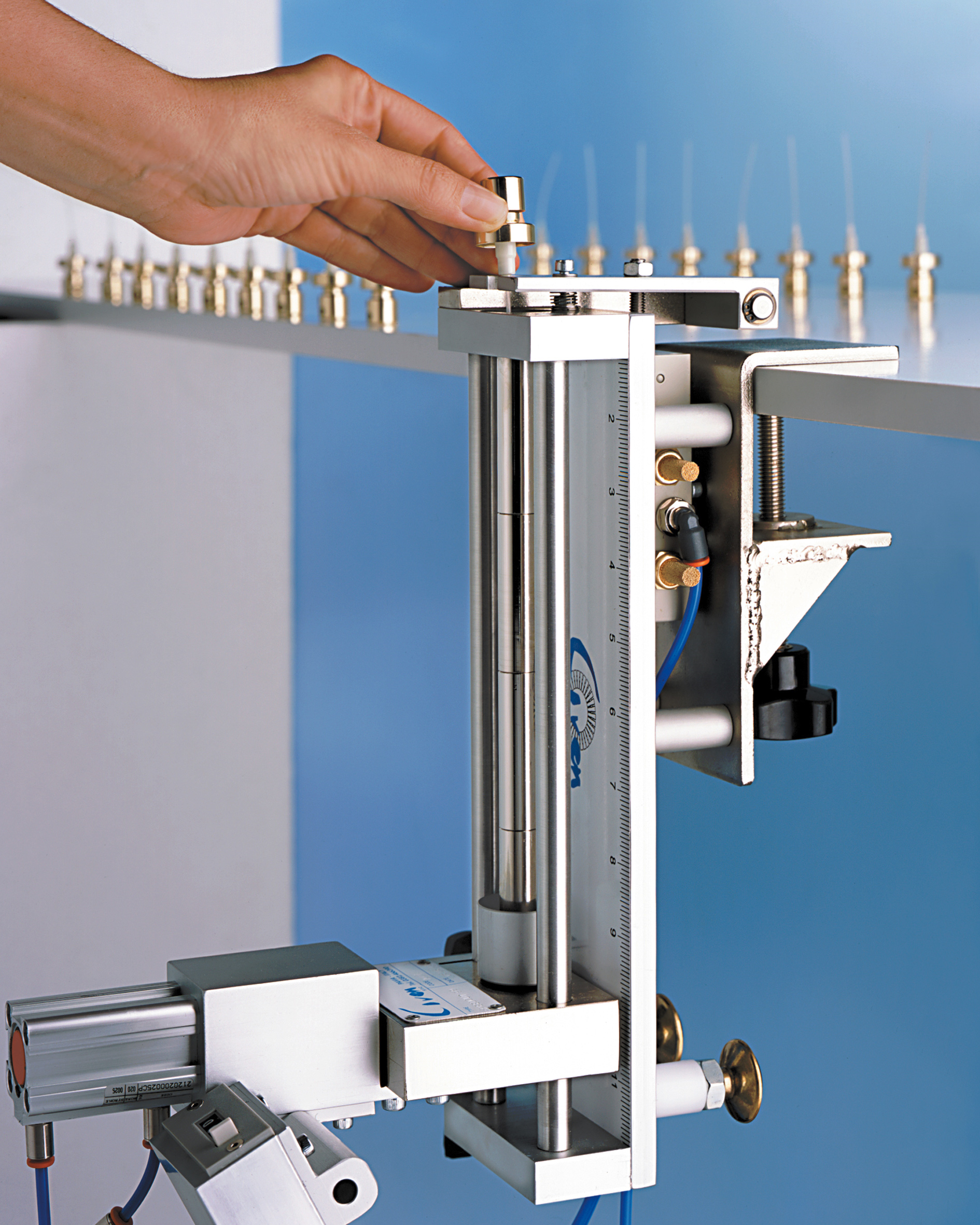 A hand adjusts a pneumatic cylinder fixture mounted to a tabletop.