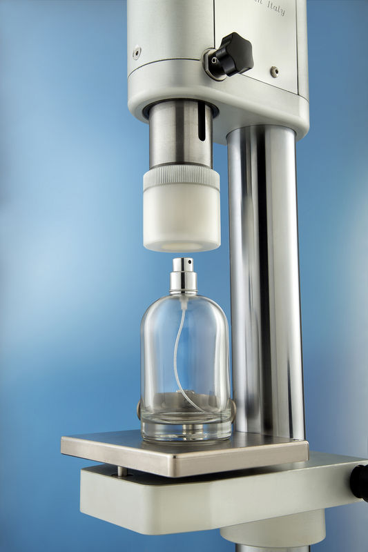 A laboratory bottle crimping machine positioned over a clear glass perfume bottle with a spray pump.