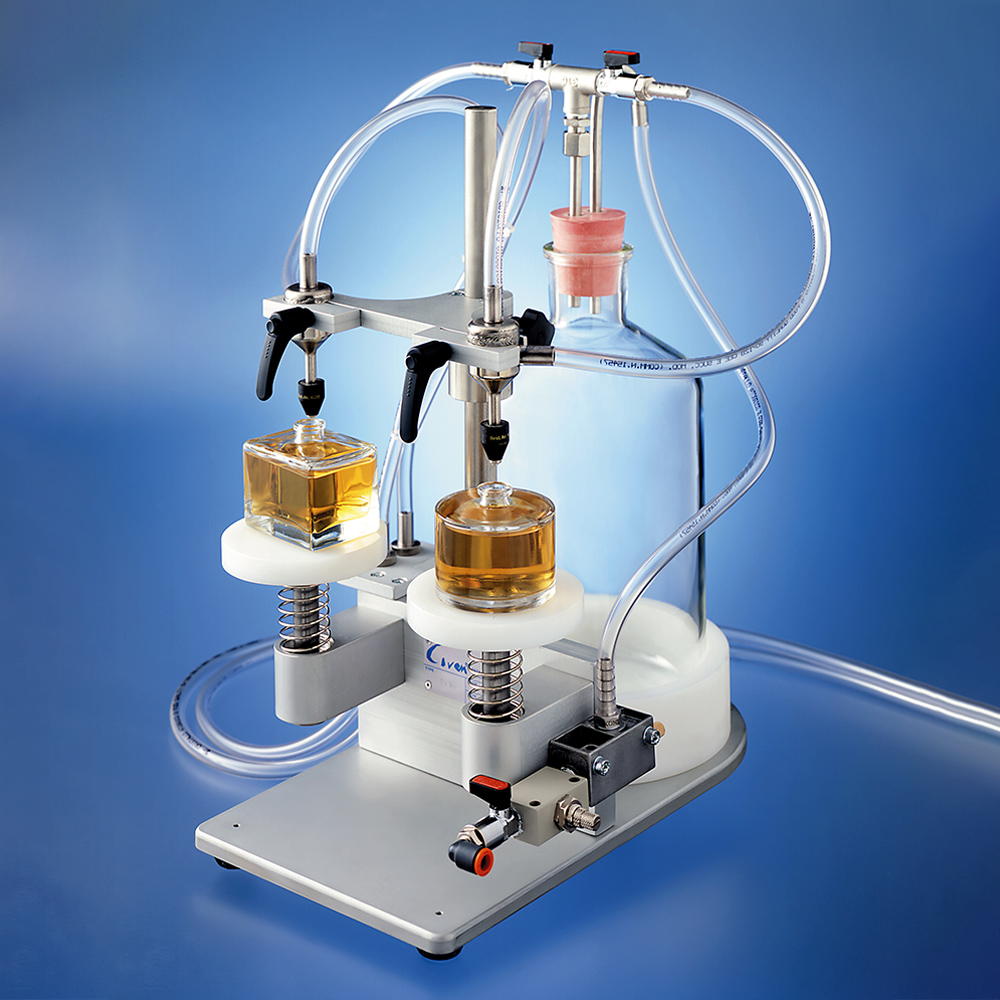 A benchtop liquid filling machine with two nozzles filling small glass bottles from a large supply reservoir.