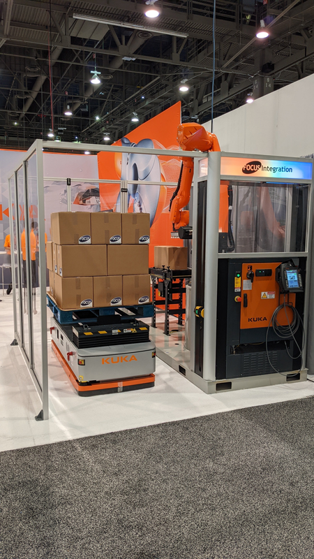 An orange robotic arm in an enclosure stacks boxes onto an automated mobile robot in a warehouse setting.