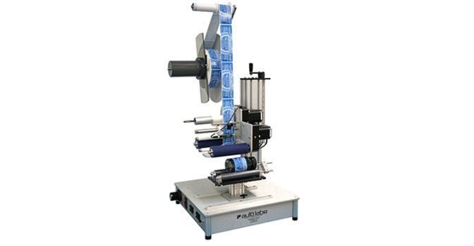 A tabletop label applicator machine with a roll of blue labels positioned on a grey platform.