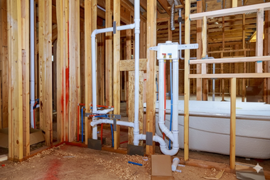 Bathroom construction with wooden framing and installed plumbing pipes.