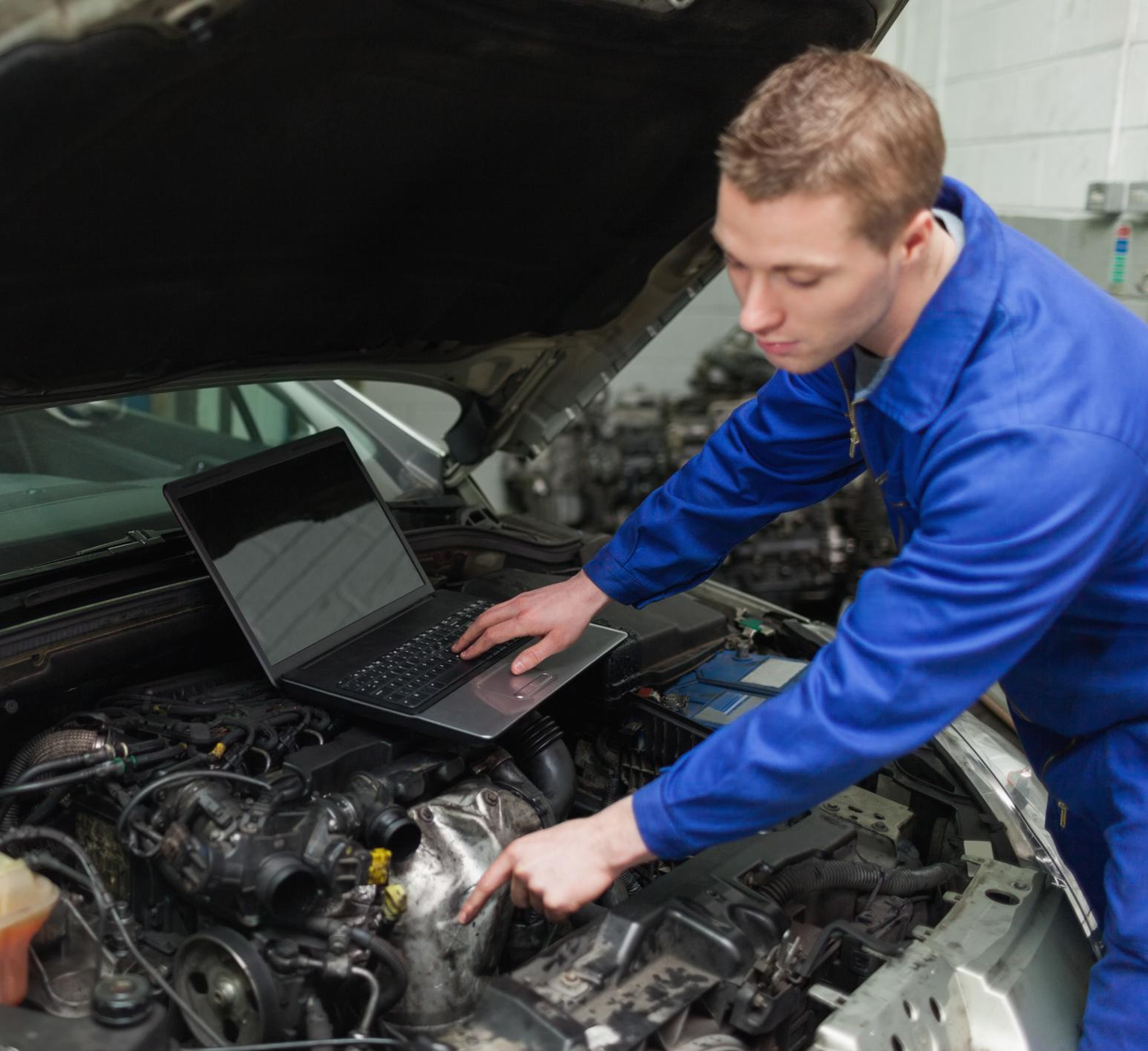 A man is working on a car engine with a laptop