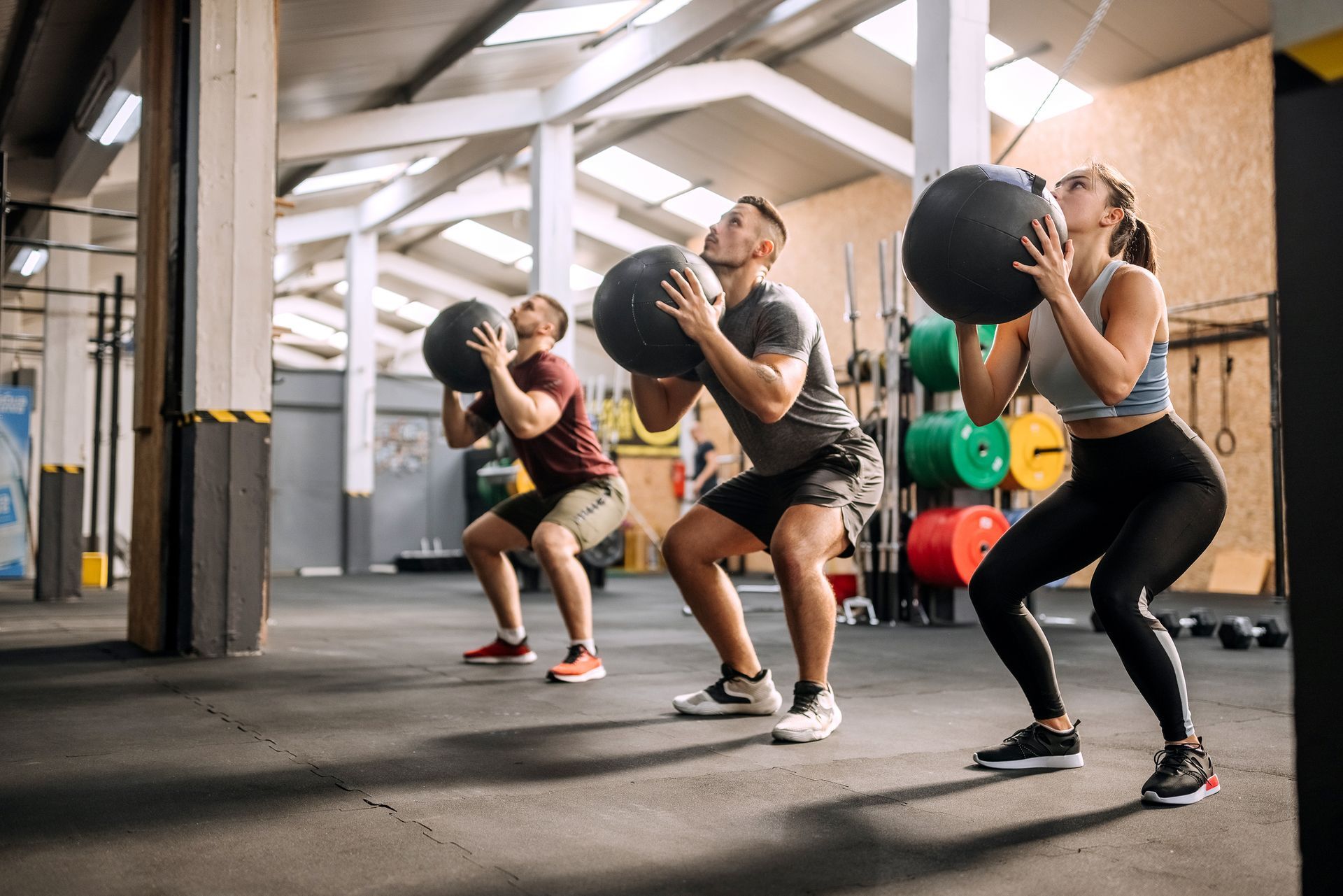A man is squatting with a medicine ball in a gym.
