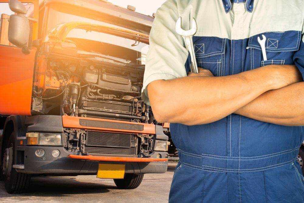 A mechanic is standing in front of a truck with his arms crossed.