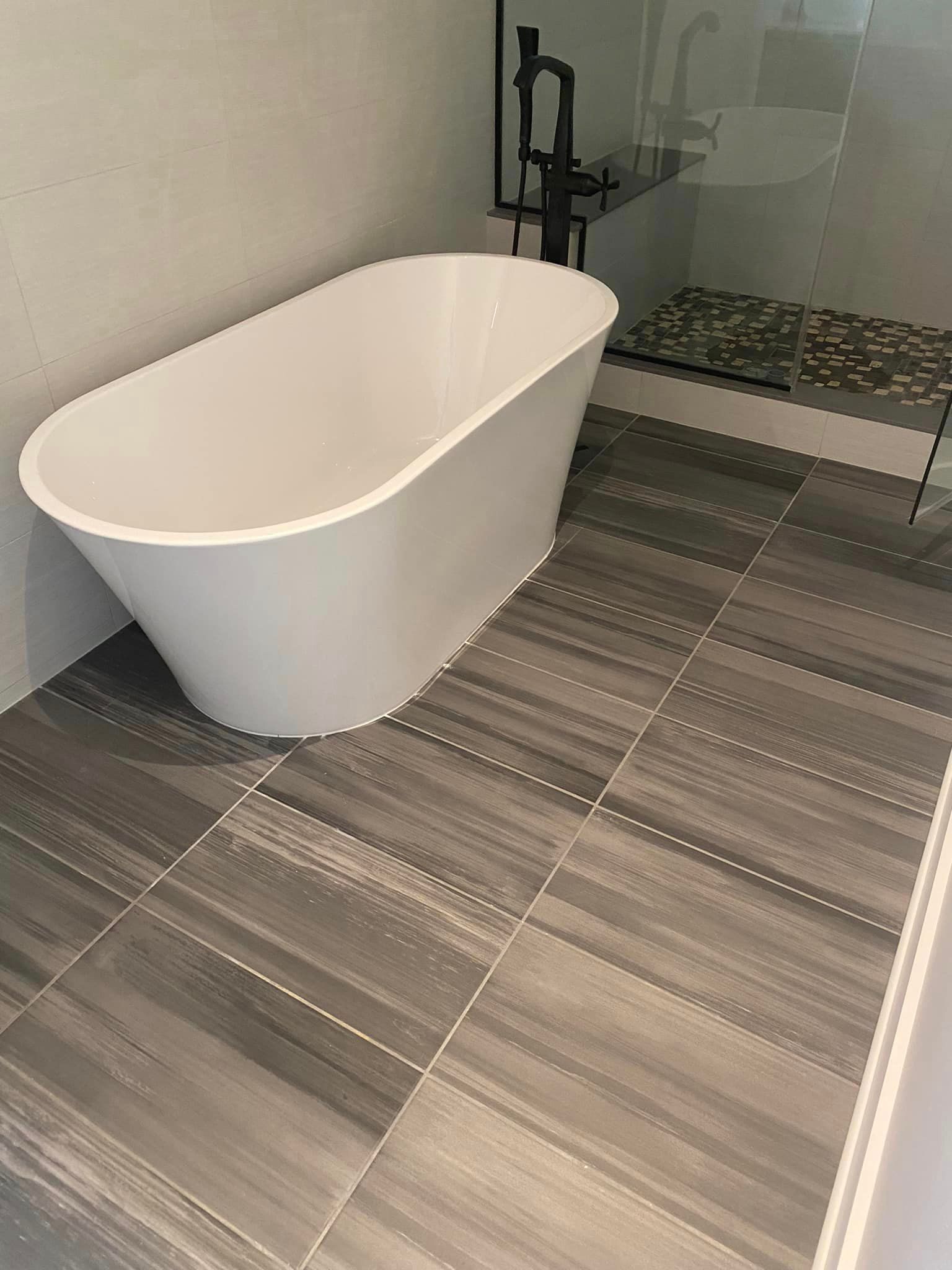 A bathtub is sitting on a tiled floor in a bathroom next to a shower by Floor Source