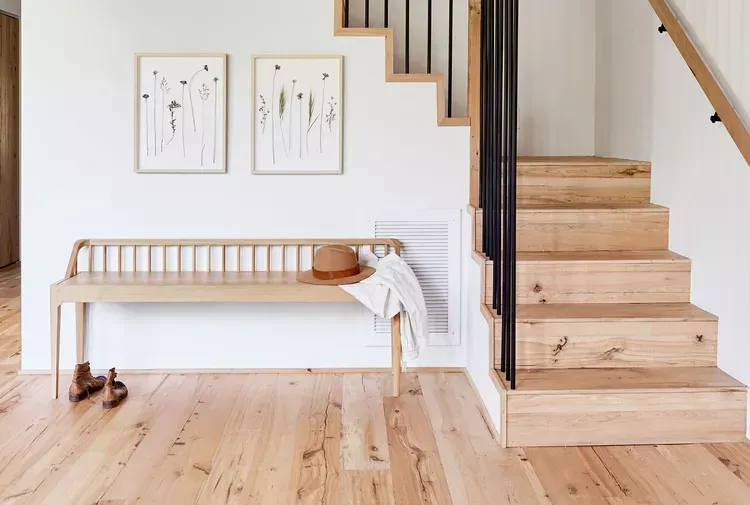 A wooden bench is sitting next to a wooden staircase in a hallway.