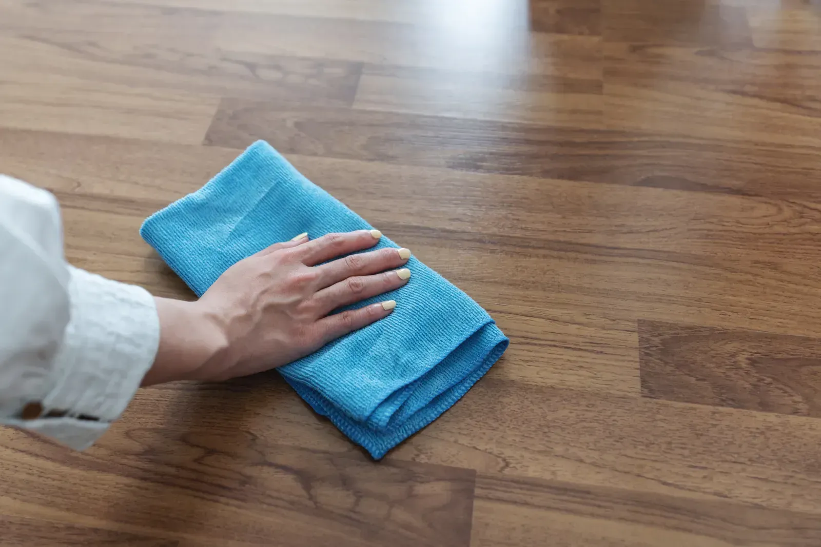 A person is cleaning a wooden floor with a blue towel.