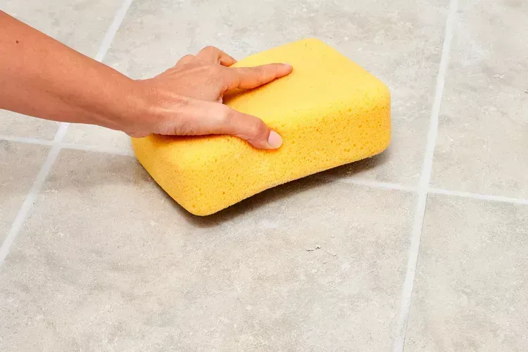 Someone cleaning a tile floor with a yellow sponge.