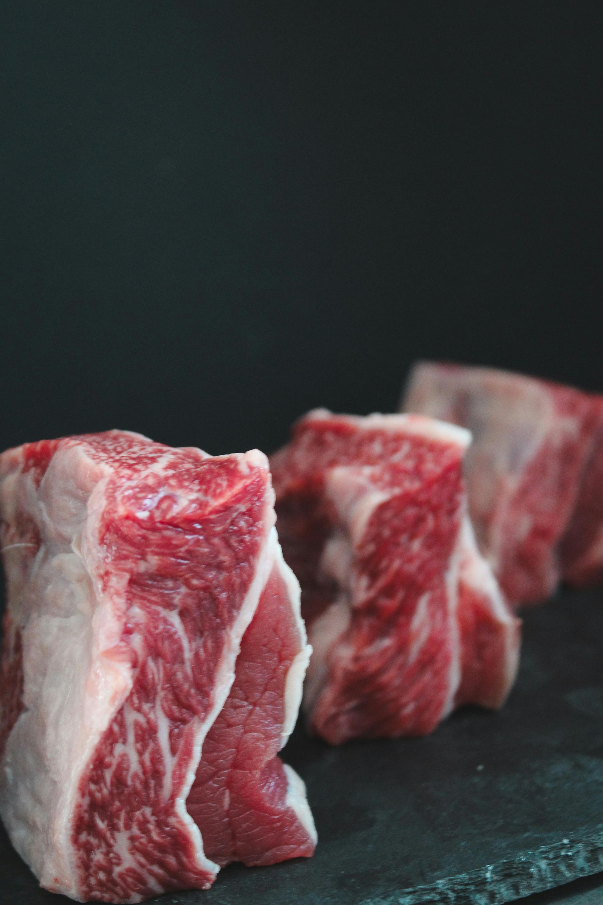Three raw, red beef short ribs on a dark slate surface.
