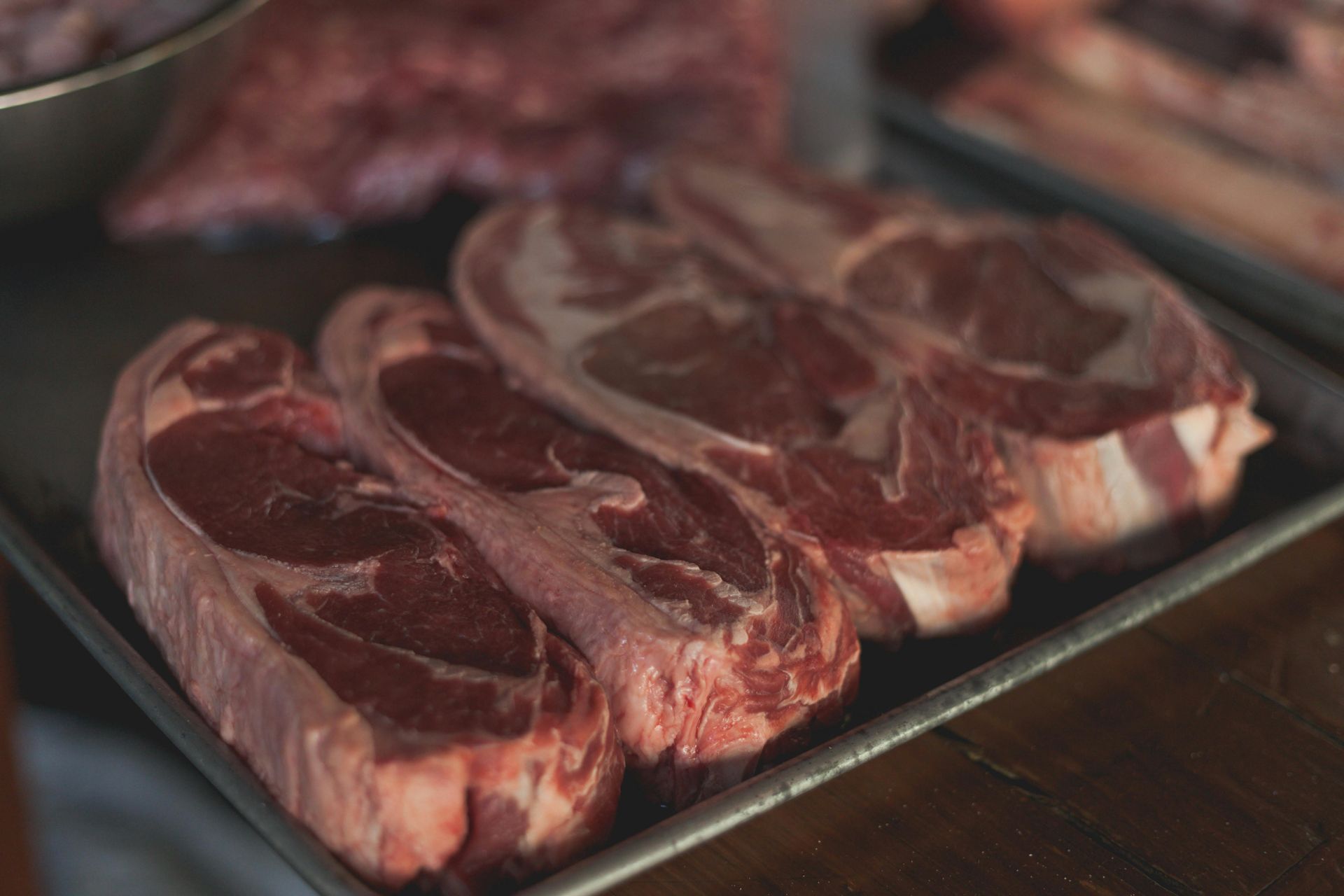 Raw steaks on a metal tray, close-up view. Red meat with visible marbling and white fat.