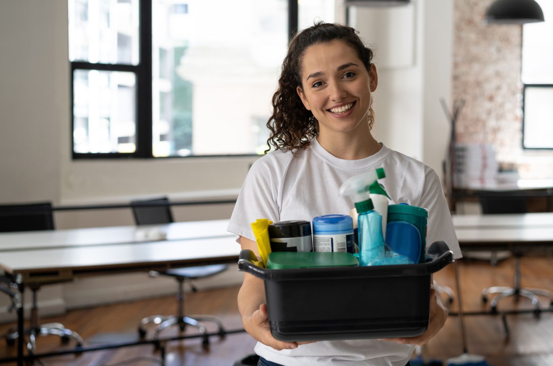 A woman is holding a bucket of cleaning supplies in an office.