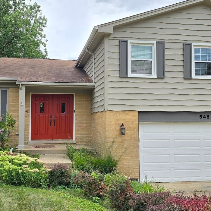 Two-story house with a red front door, gray siding, and a white garage door.