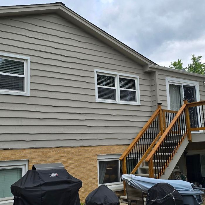 Beige house with white-framed windows, wooden deck, and a grill covered with a black cover.