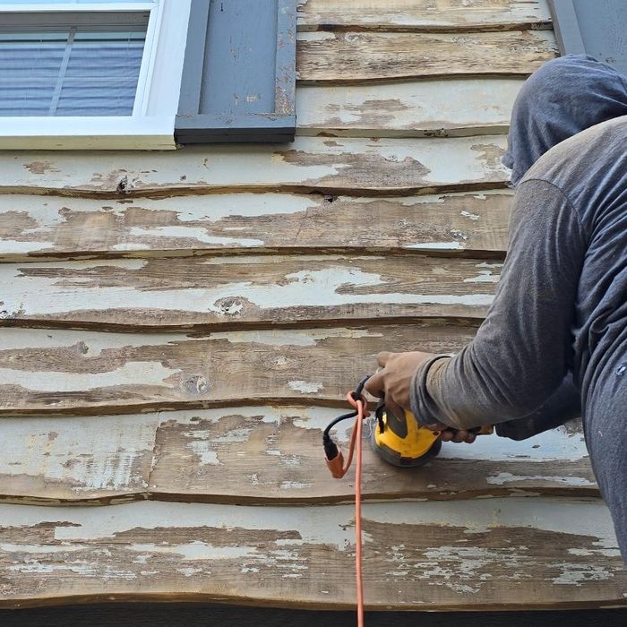 Person sanding peeling paint from wood siding on a house.