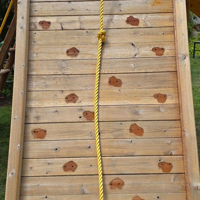 Wooden climbing wall with brown handholds and yellow rope.