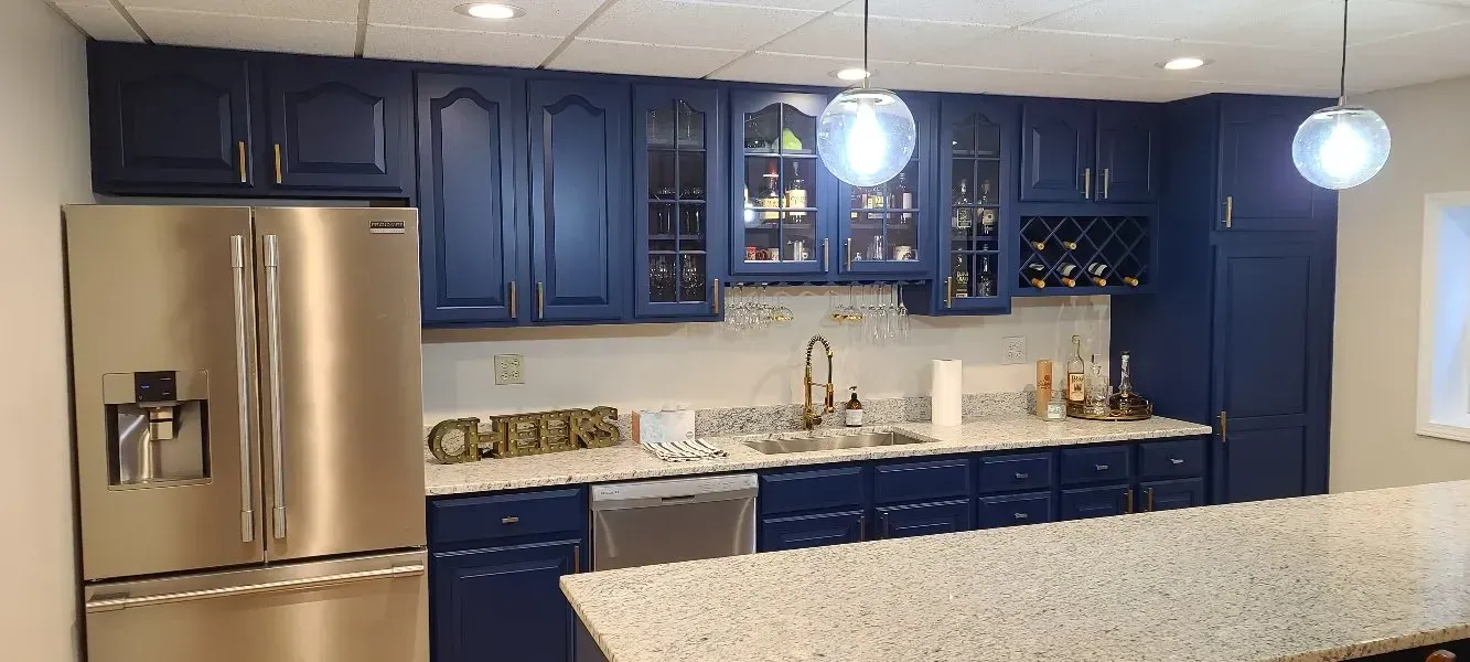 Kitchen with navy blue cabinets, stainless steel refrigerator, white countertops, and globe pendant lights.