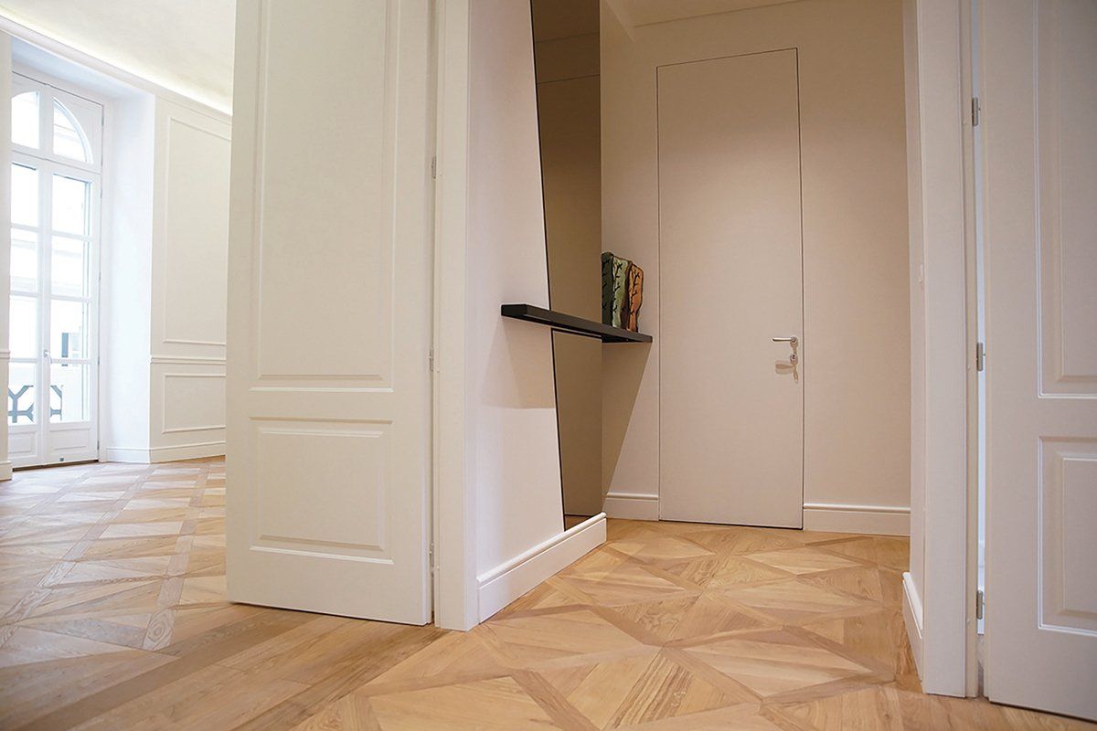 Corridoio con pavimento in legno chiaro, finiture bianche, porta e una parete marrone con mensola.