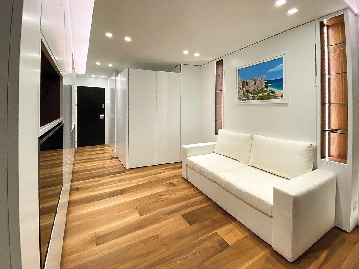 Stanza moderna con divano bianco, pavimento in legno e opere d'arte astratte; una porta nera sulla sinistra.