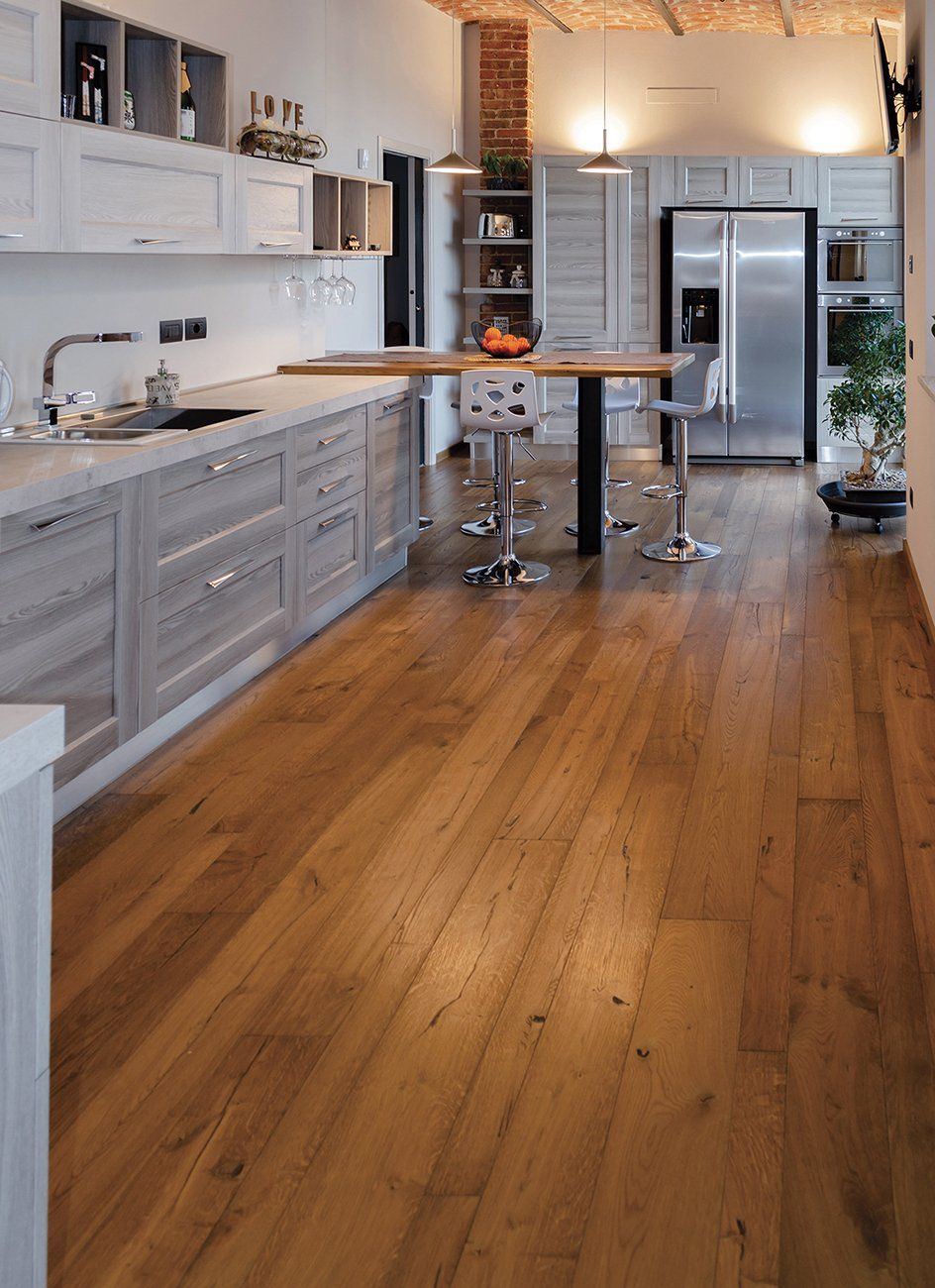 Cucina con pavimento in legno, mobili grigi, elettrodomestici in acciaio inossidabile e tavolo in legno.