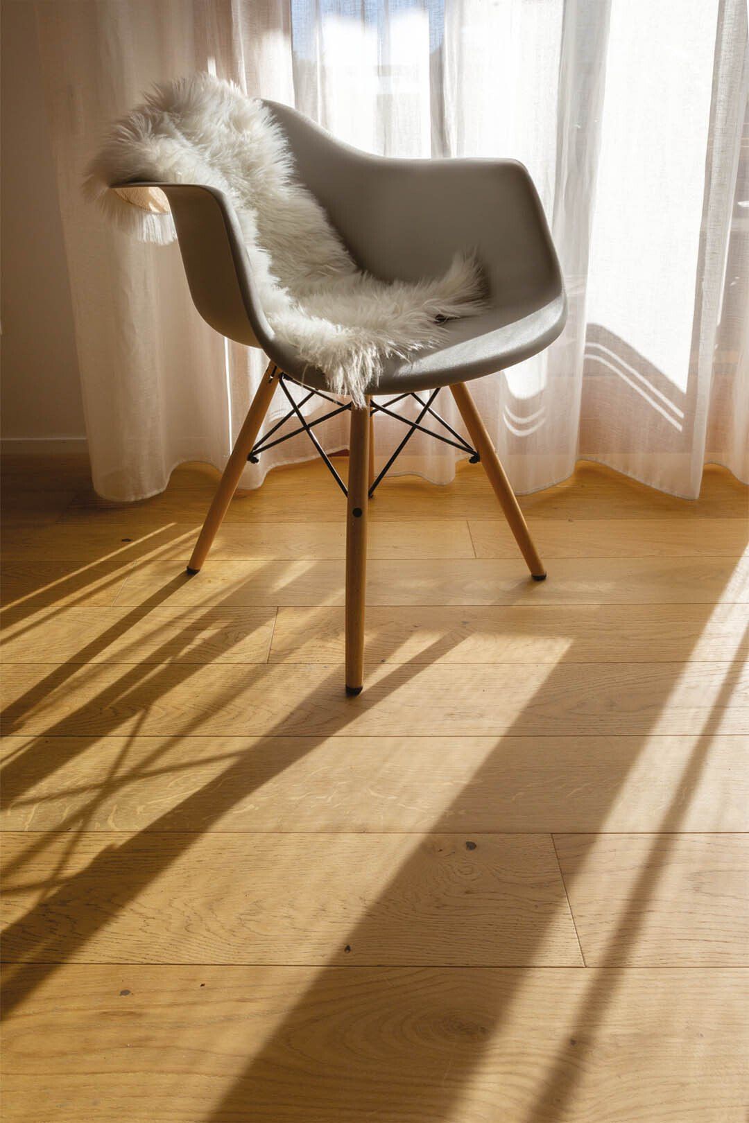 Una moderna sedia grigia con una coperta di pelliccia bianca proietta una lunga ombra sul pavimento in legno.