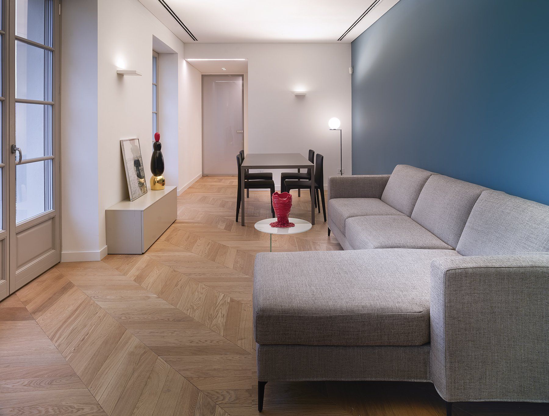 Soggiorno moderno con divano componibile grigio, parete con dettagli blu e pavimento in legno.