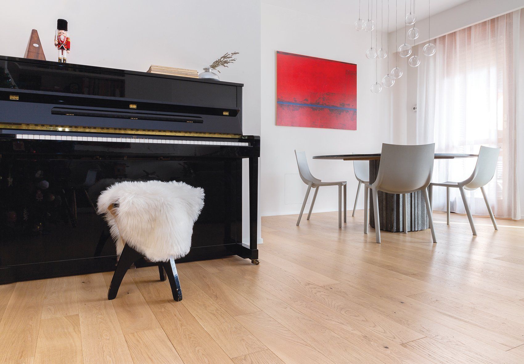 Un pianoforte nero con uno sgabello morbido accanto a un tavolo da pranzo rotondo e sedie su un pavimento in legno.