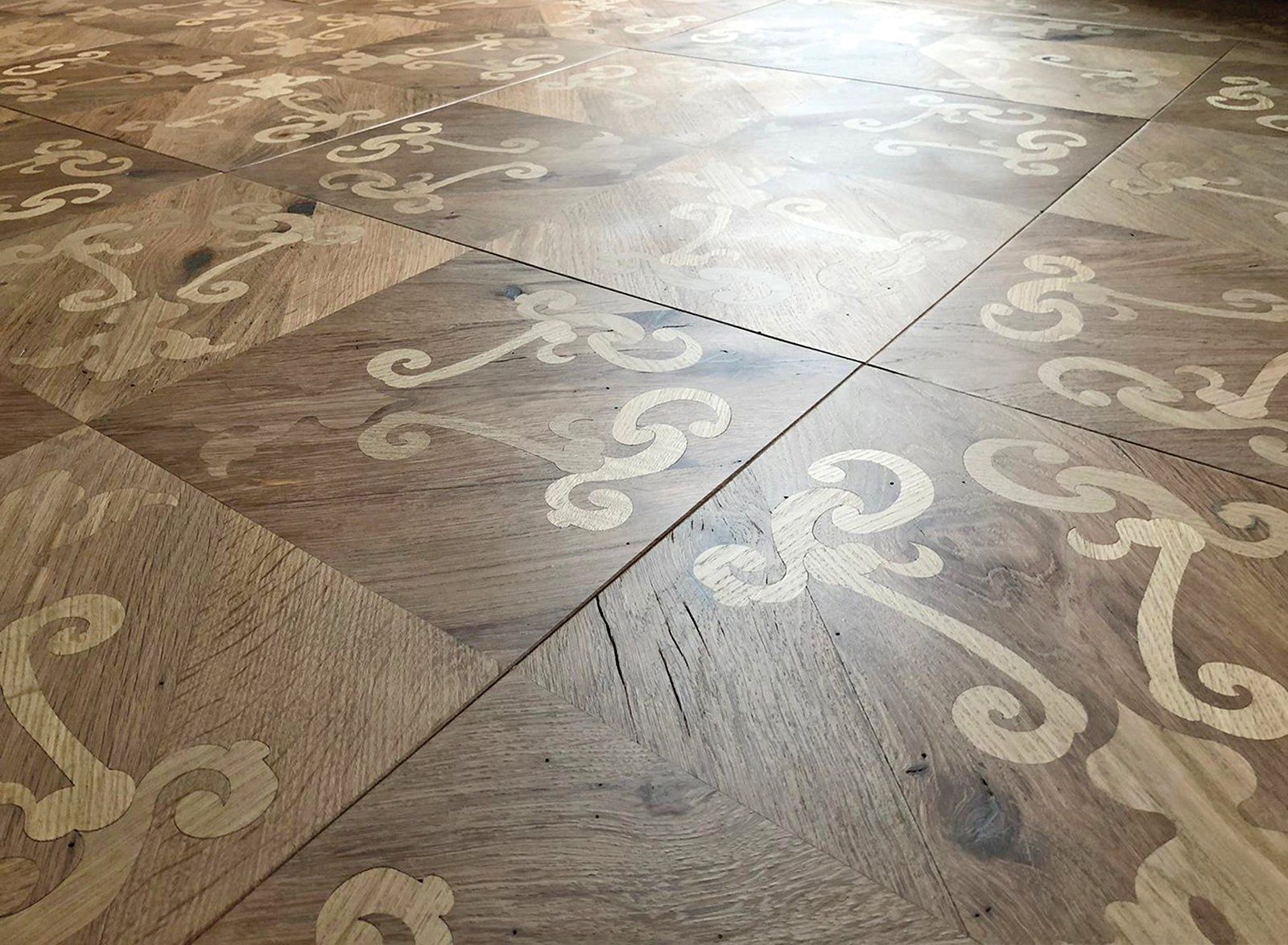 Primo piano di un pavimento in legno decorato con motivi a volute di colore chiaro.