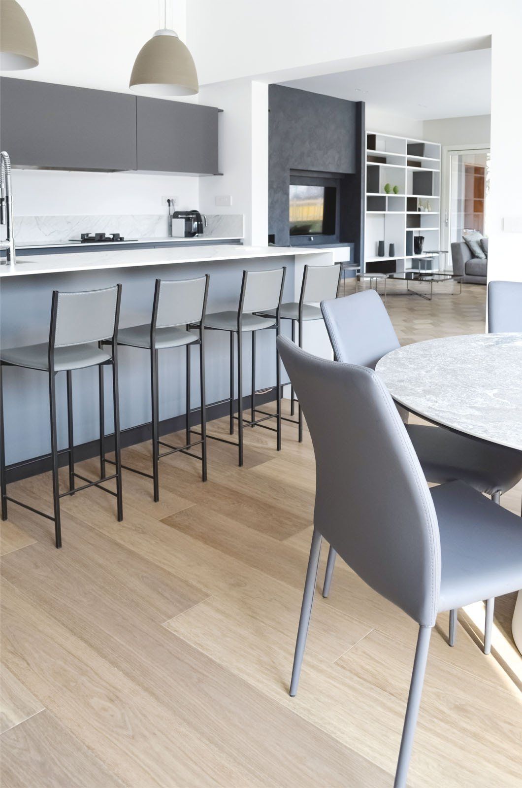 Cucina moderna con isola grigia e sgabelli da bar, tavolo da pranzo con sedie.