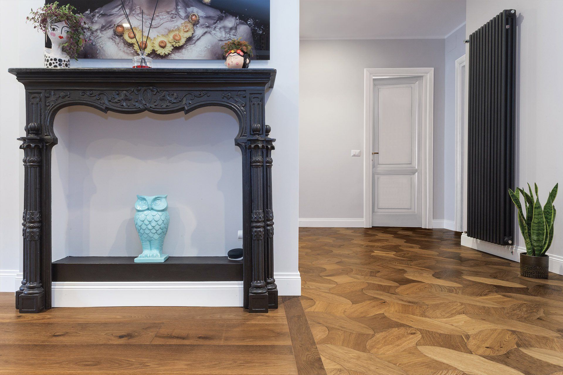 Consolle decorativa nera in un corridoio con pavimento in legno, statuetta di gufo blu e porta.