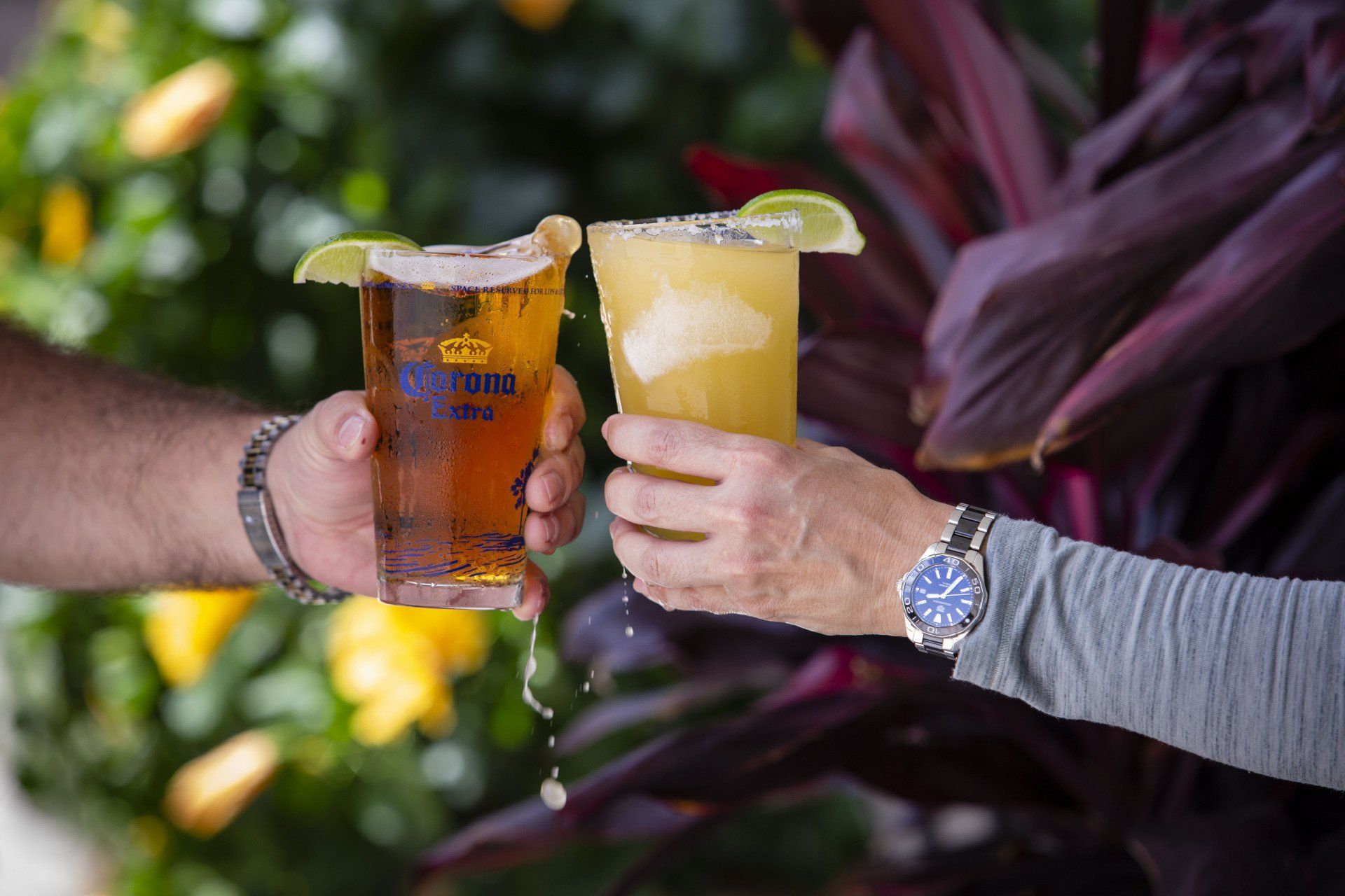 A man and a woman are toasting with beer and a margarita.
