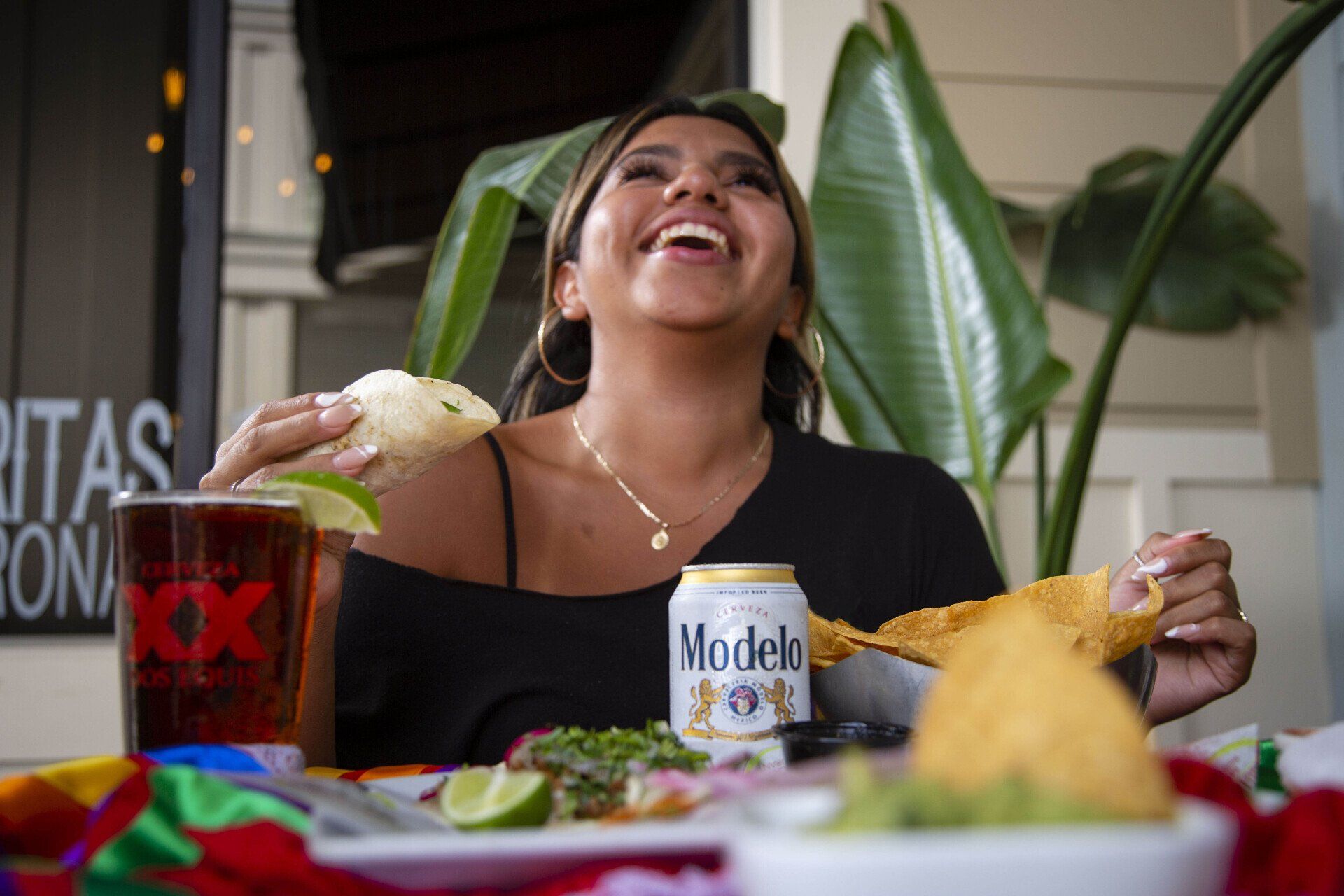 A woman is sitting at a table eating food and drinking beer.