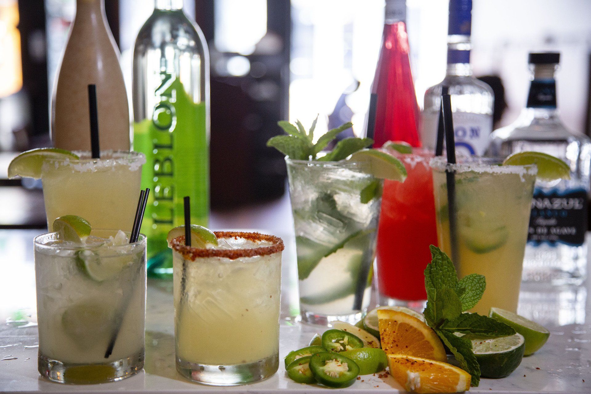 A variety of drinks are on a table with bottles in the background