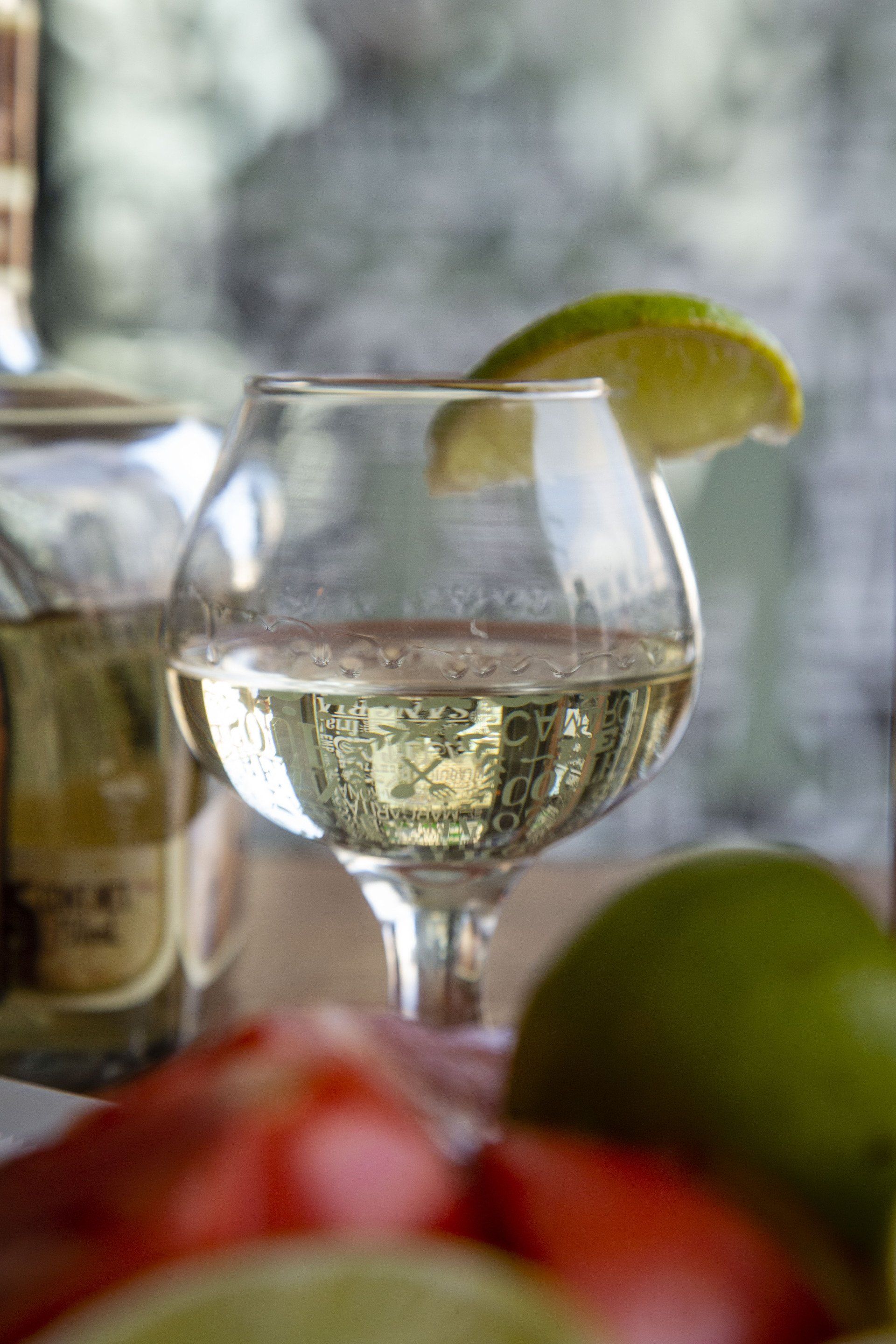 A close up of a glass of wine with a slice of lime on a table.