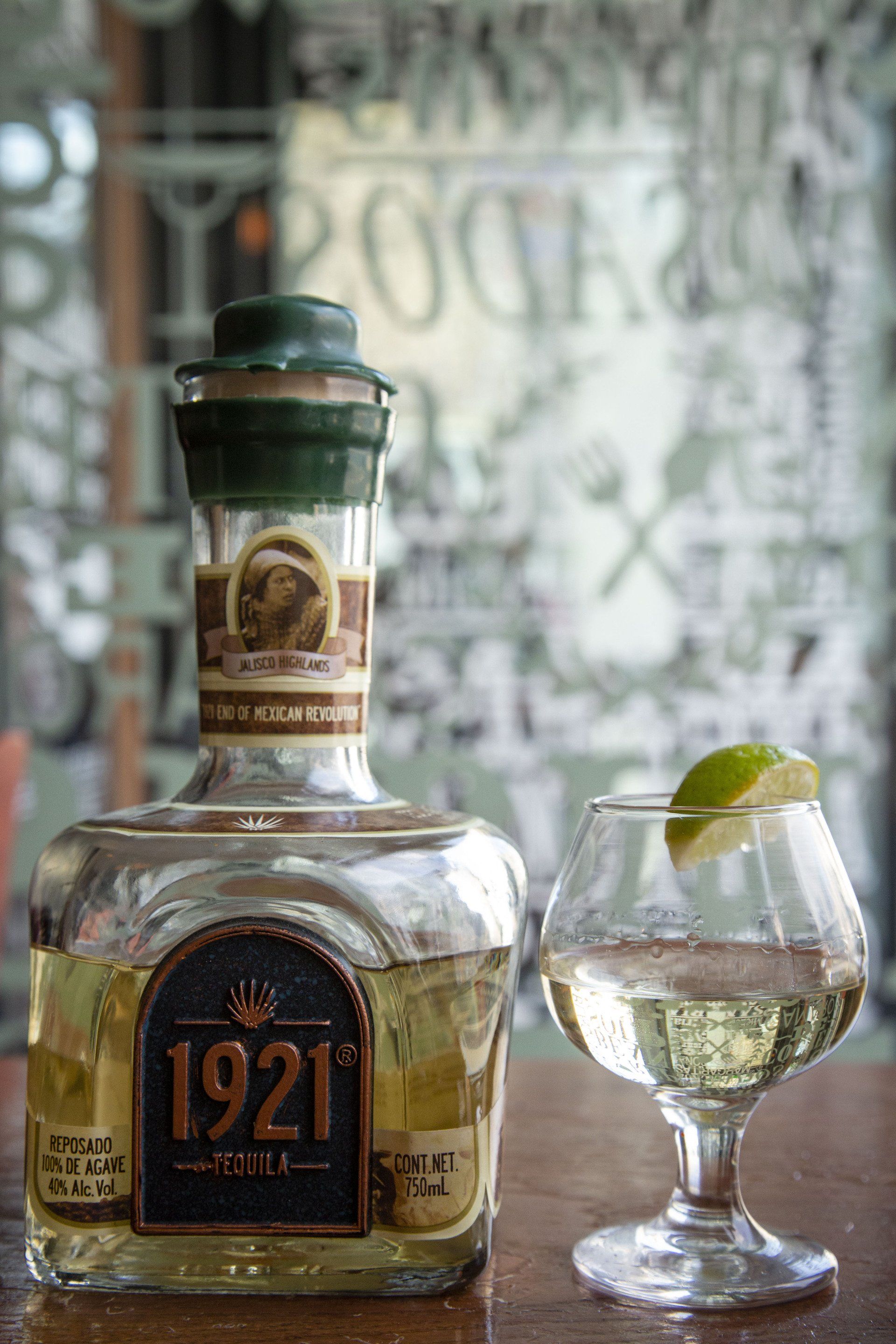 A bottle of tequila and a glass of tequila on a bar.