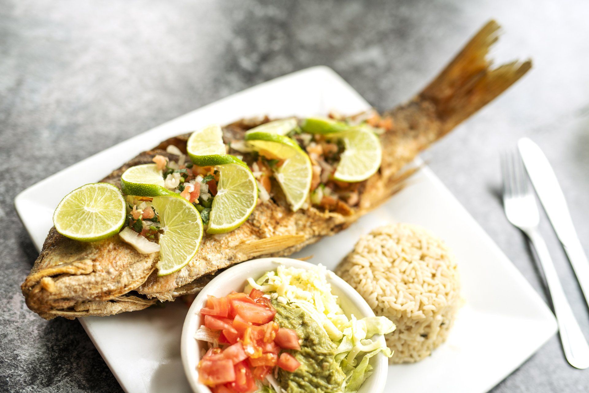 A white plate topped with a fish , rice , and vegetables.