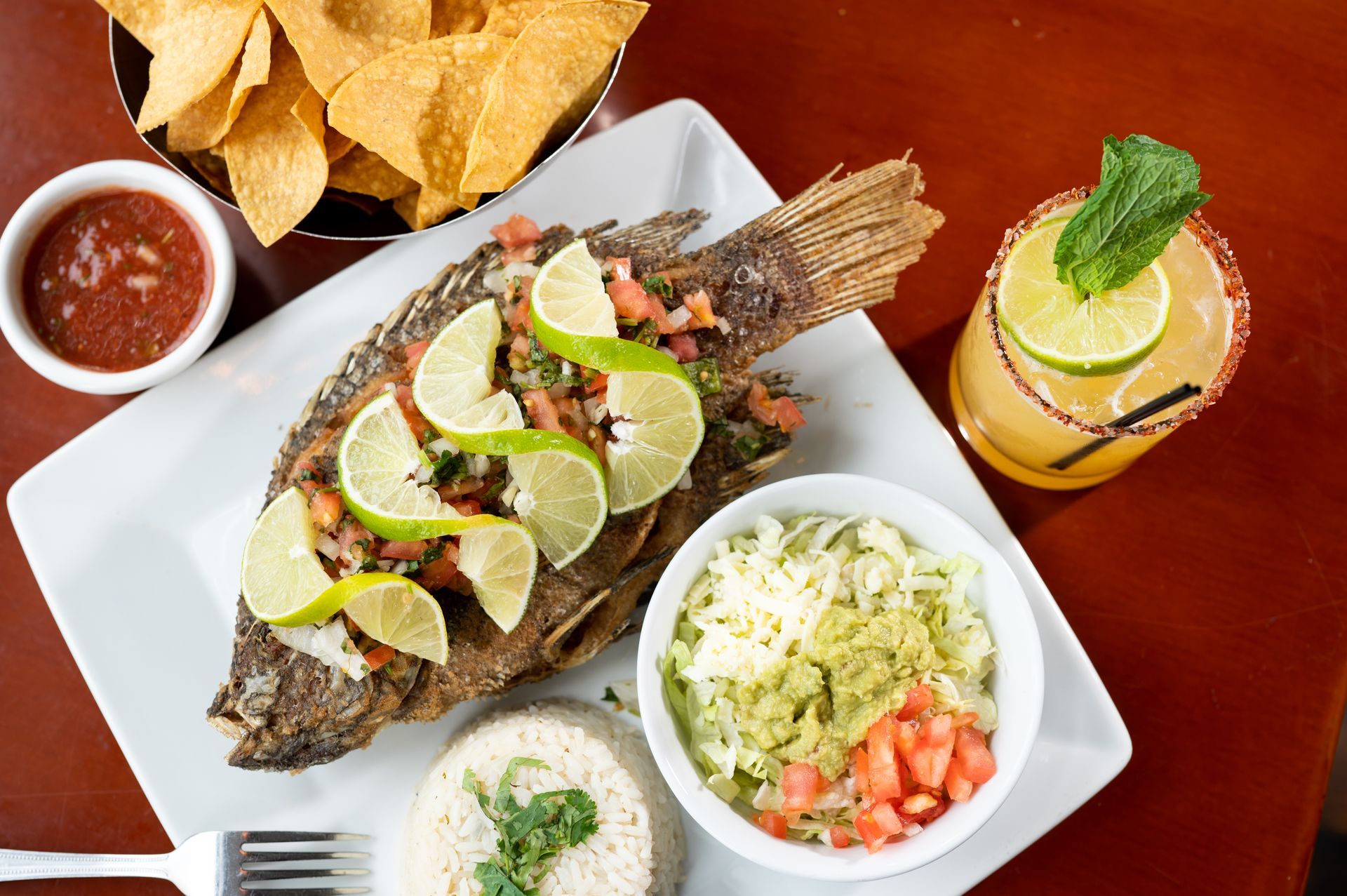 A plate of food with a fish , rice , guacamole and salsa on a table.