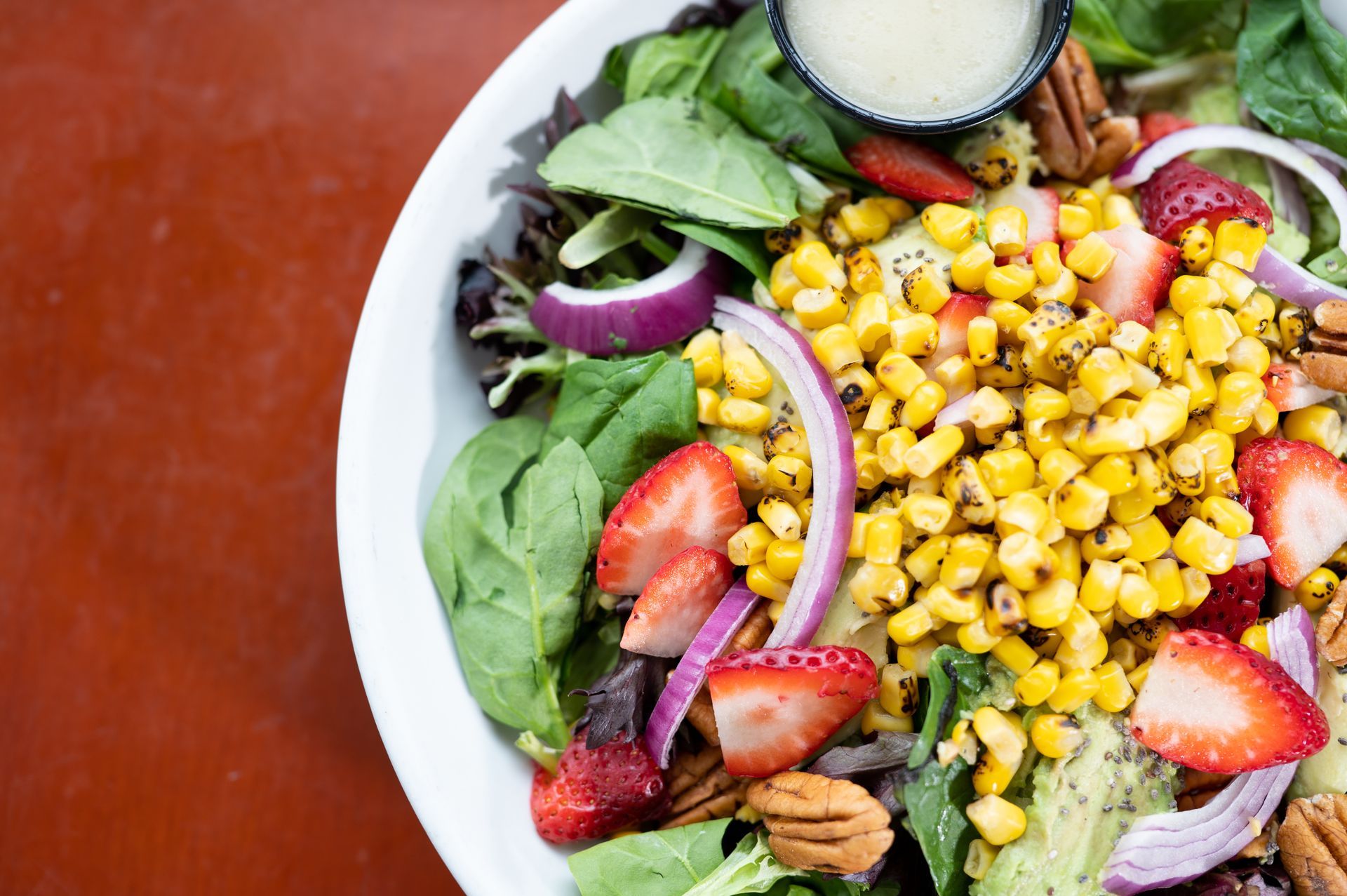 A salad with corn , strawberries , onions and pecans in a bowl on a table.