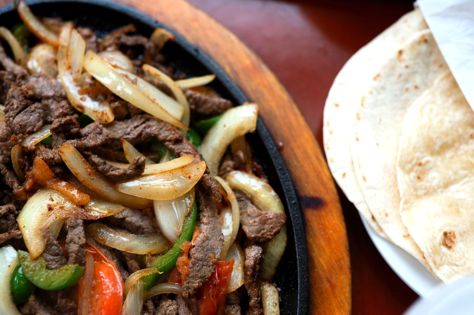 A plate of food with meat and vegetables next to a tortilla.
