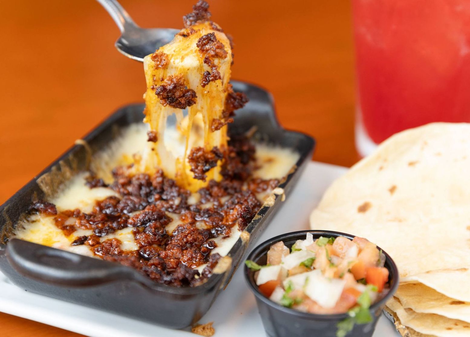 A person is dipping a piece of food into a bowl of cheese and chorizo.