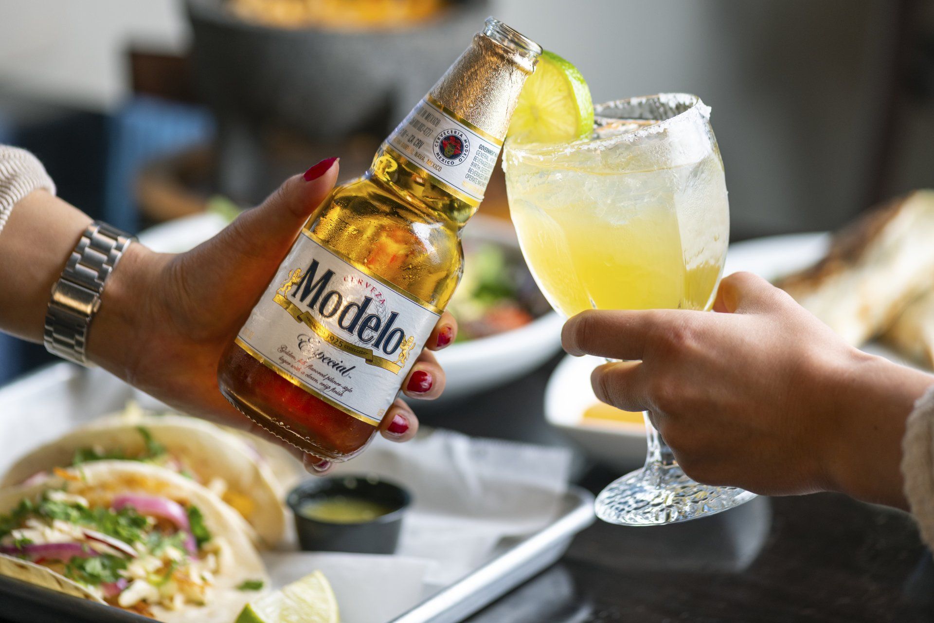 A person is holding a bottle of modelo beer and a glass of margarita.