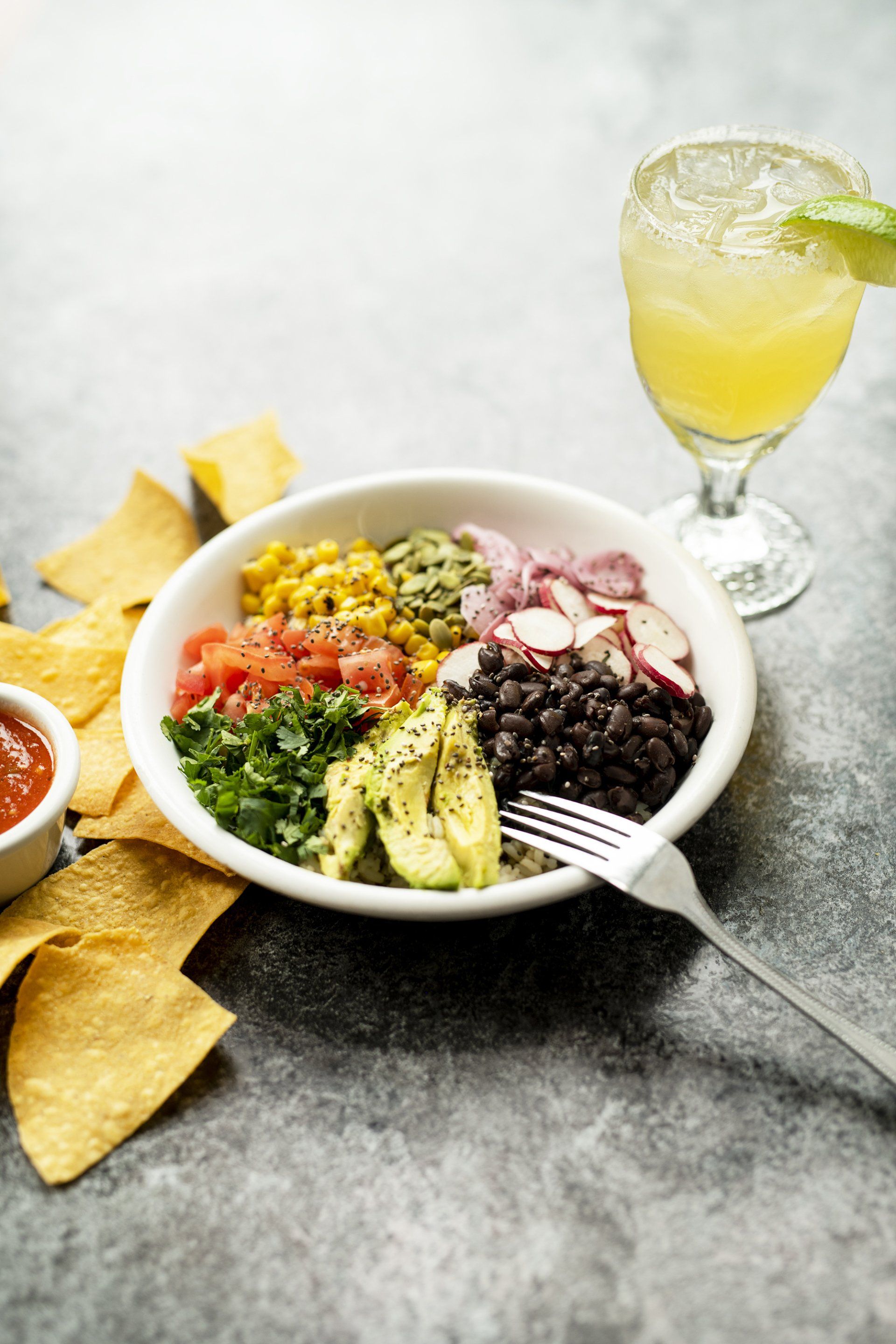 A bowl of food with a fork and a margarita on a table.