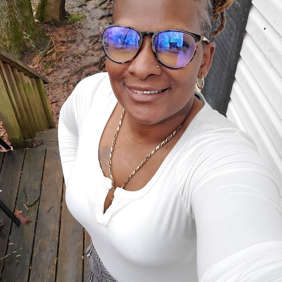 A woman wearing sunglasses and a white shirt is taking a selfie