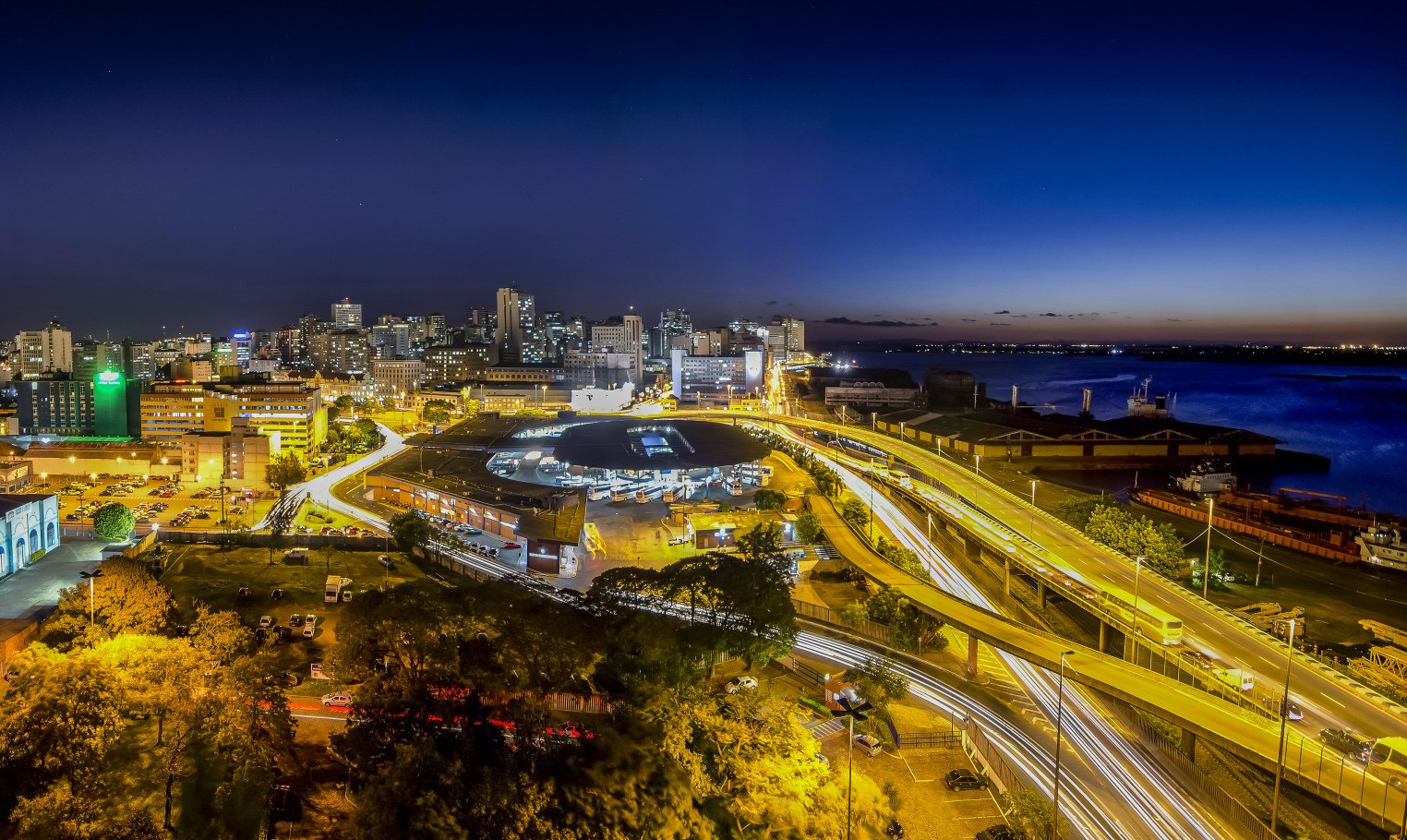 Uma vista aérea de uma cidade à noite com um corpo de água ao fundo.