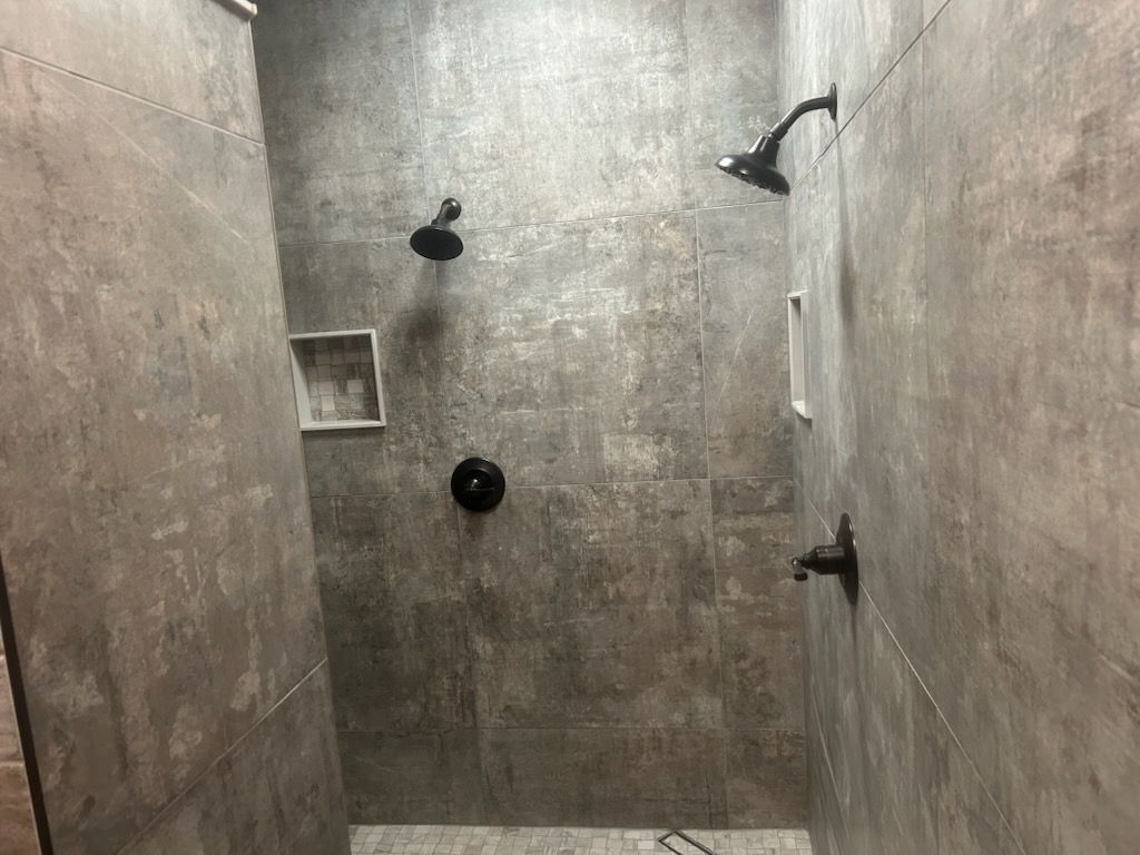 A shower with two shower heads and a gray tile wall.