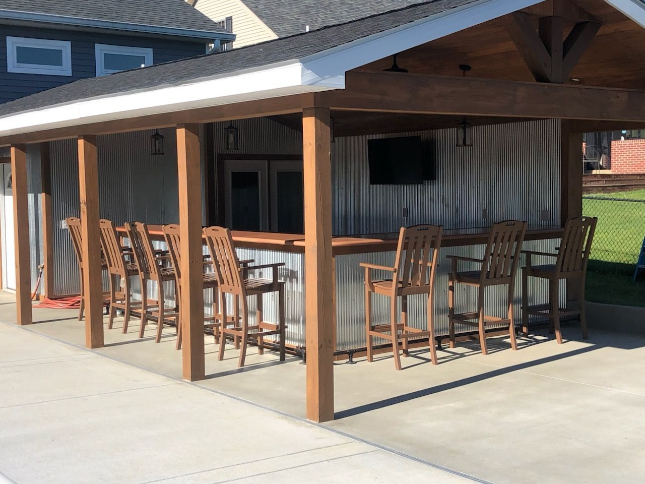 A covered patio with a bar and chairs under a roof.