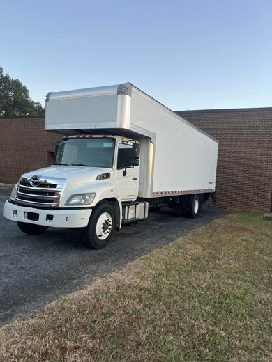 A white moving truck is parked in front of a brick wall.