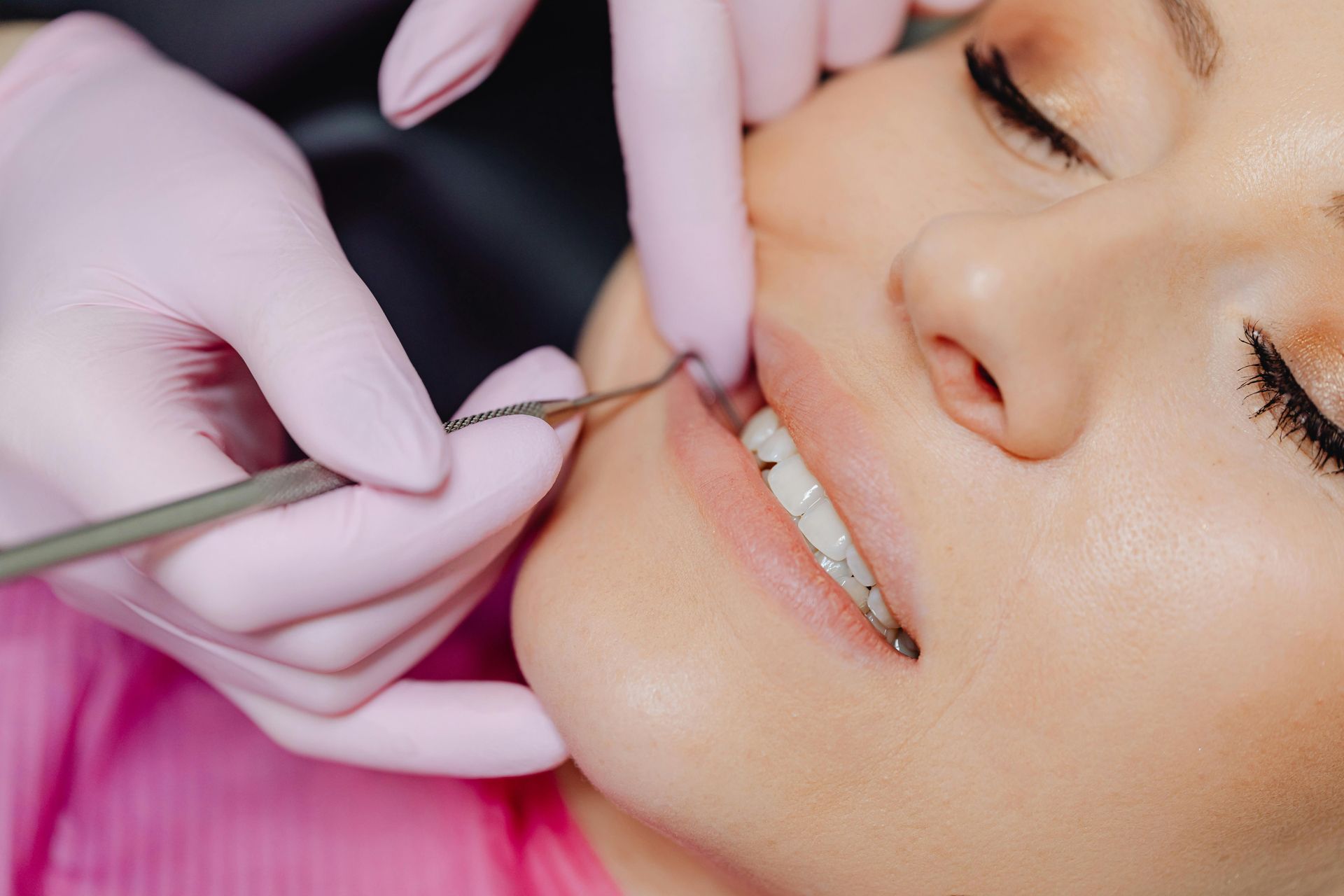 Person's mouth being examined by someone wearing pink gloves, using dental tools.