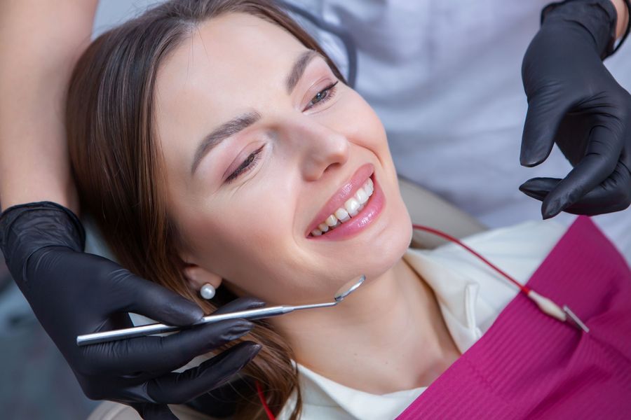 Woman in dental chair smiling, dentist with black gloves and dental tools.